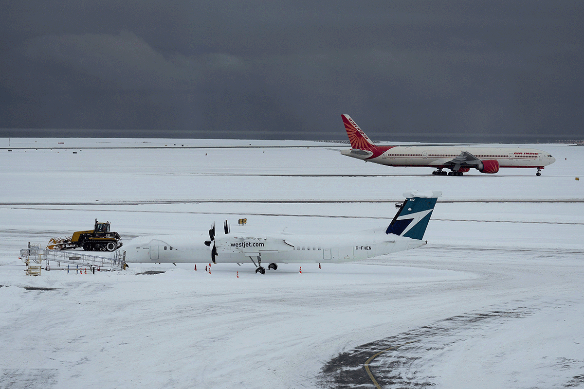 A worker clears snow from the apron as Westjet and Air India aircraft sit idle at Vancouver International Airport after a snowstorm crippled operations leading to cancellations and major delays, in Richmond, British Columbia, on Tuesday, Dec. 20, 2022. 