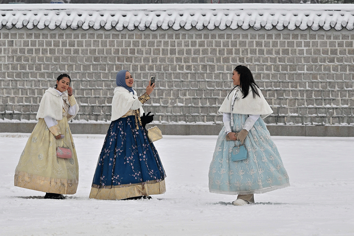 Visitors wearing traditional hanbok dress take photos at Gyeongbokgung Palace covered in snow in Seoul on December 21, 202