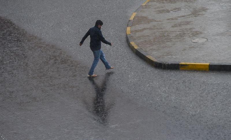 A resident crossing the street as rain pours down in Sharjah, Al Khan.