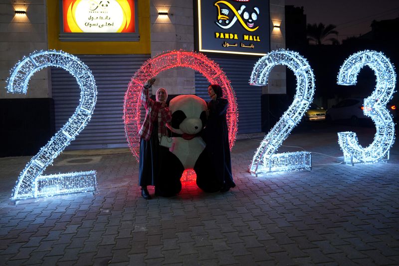 Palestinian women take photos of themselves in front of giant panda decorations and illuminated numbers for the new year 2023, at the main road in Gaza City 