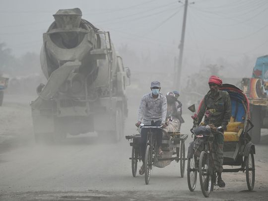 Commuters make their way along a street amid dusty conditions in Dhaka 