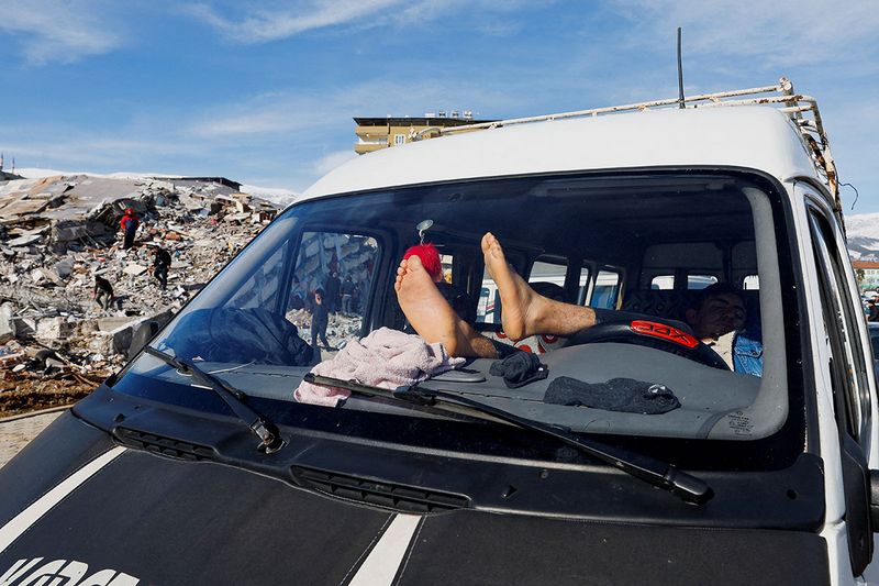 A person sleeps in a vehicle parked near the site of a collapsed building in the aftermath of an earthquake in Kahramanmaras, Turkey, February 7, 2023