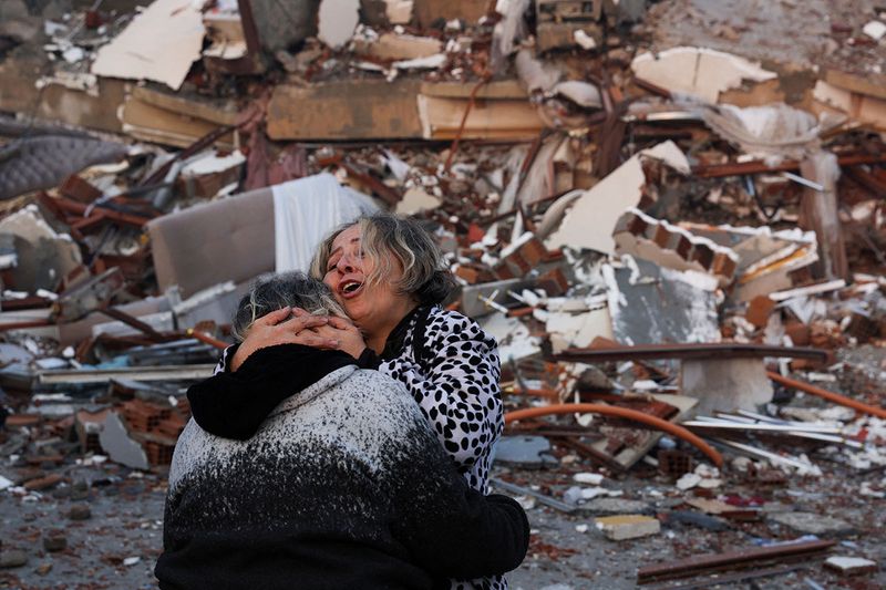 A woman reacts while embracing another person, near rubble following an earthquake in Hatay, Turkey, February 7, 2023.