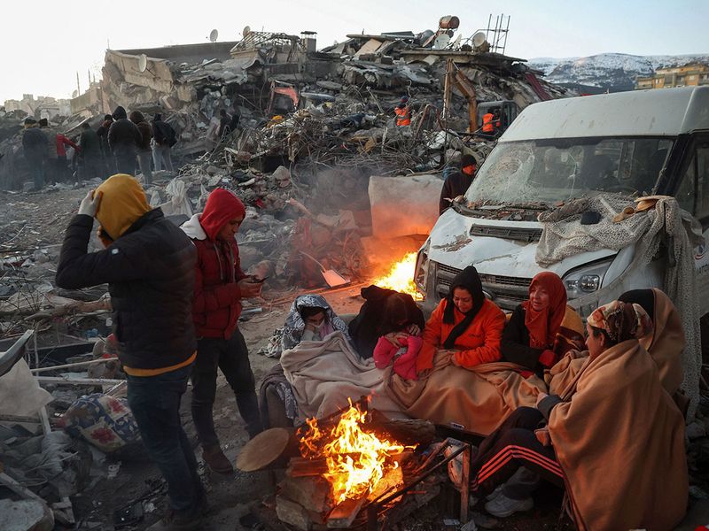 TOPSHOT - Survivors gather next to a bonfire outside collapsed buildings in Kahramanmaras.