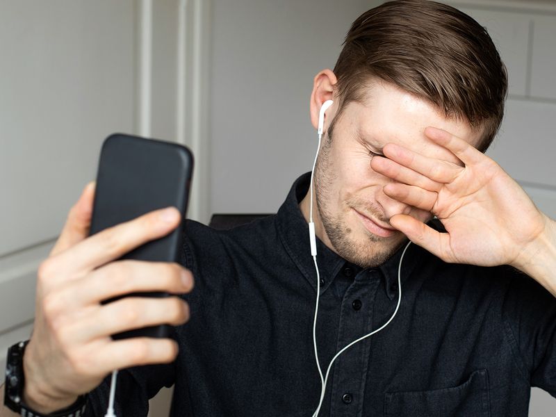 Person covering their eyes while using phone