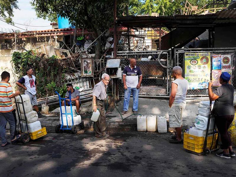 Locals wait for their turn to fill their water containers from water collected in an abandoned highway tunnel at the Cotiza neighborhood of Caracas, Venezuela, March 20, 2023.