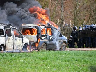 French gendarmes' stand next to gendarmes' cars burning on the sideline of a demonstration called by the collective 