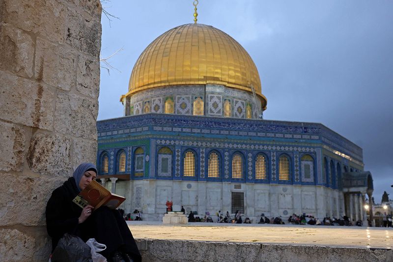A woman reads from the Quran outside the Dome of the Rock shrine at Al-Aqsa mosque compound, during the Muslim holy fasting month of Ramadan in Jerusalem on March 29, 2023.