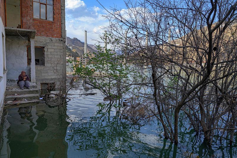 A local resident looks on, as she returned to her flooded home to attempt to retrieve belongings in the town of Yusufeli, submerged by an artificial lake caused by a dam retaining the flow of the Coruh river (also referred to as Chorokhi), Artvin province, in northeastern Turkey, on April 5, 2022. - The Yusufeli Dam and its Hydroelectric Power Plant Project in the Eastern Black Sea Region has started to hold water, with the electricity production expected to start in May 2023. With a total water storage volume of approximately 2.2 billion cubic meters, the double curvature concrete arch dam is Turkey’s highest with a height of 275 meters. 