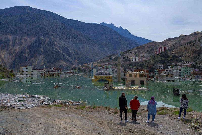 Local residents look on at their town, Yusufeli, submerged by an artificial lake caused by a dam retaining the flow of the Coruh river (also referred to as Chorokhi), Artvin province, in northeastern Turkey, on April 4, 2022. - The Yusufeli Dam and its Hydroelectric Power Plant Project in the Eastern Black Sea Region has started to hold water, with the electricity production expected to start in May 2023. With a total water storage volume of approximately 2.2 billion cubic meters, the double curvature concrete arch dam is Turkey’s highest with a height of 275 meters