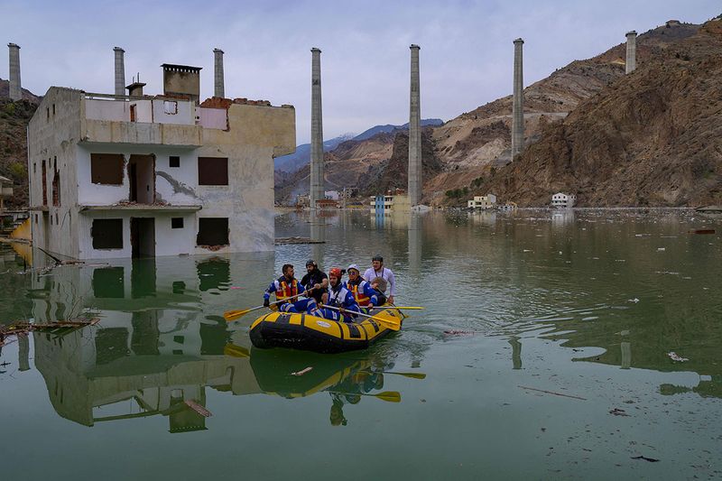Volonteers from an animal rights NGO Haytap paddle a dinghy as they search for stray cats an dogs to rescue in the town of Yusufeli as it is gradually submerged by an artificial lake caused by a dam retaining the flow of the Coruh river (also referred to as Chorokhi), in Yusufeli, Artvin province, in northeastern Turkey, on April 4, 2022. - The Yusufeli Dam and its Hydroelectric Power Plant Project in the Eastern Black Sea Region has started to hold water, with the electricity production expected to start in May 2023. With a total water storage volume of approximately 2.2 billion cubic meters, the double curvature concrete arch dam is Turkey’s highest with a height of 275 meters. 