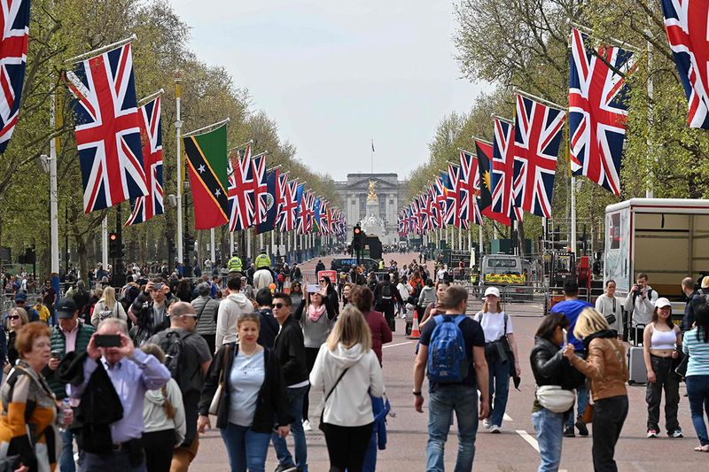 People walk beneath flags of the Union and Commonwealth along The Mall, towards Buckingham Palace, in central London, on April 30, 2023 ahead of the coronation ceremony of Charles III and his wife, Camilla, as King and Queen of the United Kingdom and Commonwealth Realm nations, on May 6, 2023.