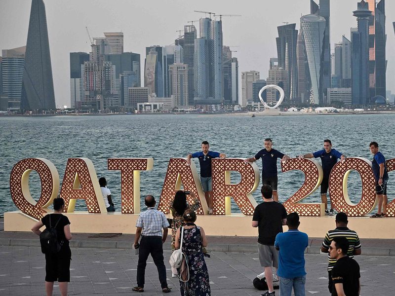 In this file photo taken on December 03, 2022 People pose for photos at the Corniche promenade as Doha's skyline is seen in the background during the Qatar 2022 World Cup football tournament. - Months after hundreds of thousands of football fans packed into its hotels and stadiums, Qatar is seeking to remedy a bout of the post-World Cup blues by hosting more international events. Along with the departed football crowds, thousands of foreign workers left the Gulf state after Lionel Messi lifted the coveted trophy on December 18. Many of those who stayed on are counting the cost.