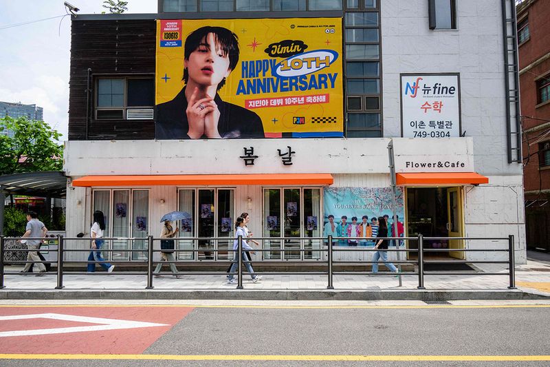 Pedestrians walk past posters celebrating the 10-year anniversary of K-pop megastars BTS.