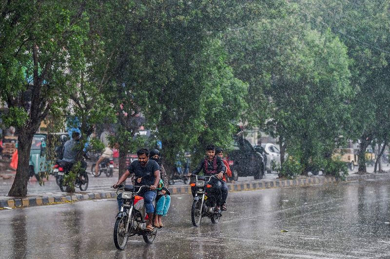 Commuters make their way amid rain showers in Karachi on June 15, 2023.