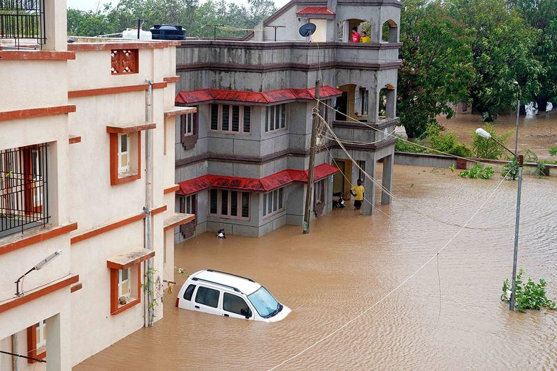 Residents watch as a car drowns in an inundated street at the coastal town of Mandvi as cyclone Biparjoy makes landfall on June 16, 2023. Cyclone Biparjoy tore down power poles and uprooted trees on June 16 after pummelling the Indian coastline, though the storm was weaker than feared and there were no immediate reports of casualties.