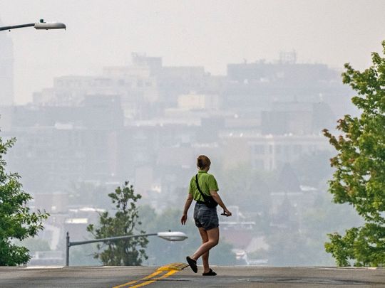 A woman crosses a street as smoke from the Canadian wildfires renders the cityscape amorphous in Washington, DC. 