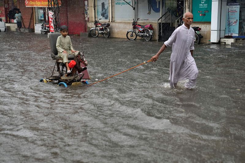 A man pulls a handcart carrying a boy as they wade through a flooded road in Lahore.  The monsoon season officially started this week and will continue until September in the South Asian country.