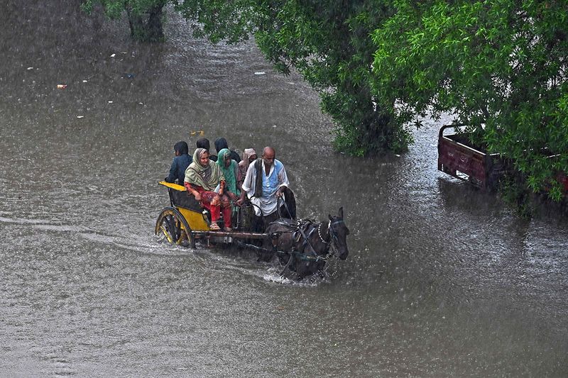 People ride on a horsecart through a flooded street after heavy rainfall in Lahore on July 5, 2023.