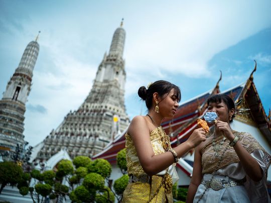 Women dressed in traditional Thai costumes eat ice creams shaped like tiles of the famous Wat Arun temple, or Temple of Dawn, in Bangkok. 