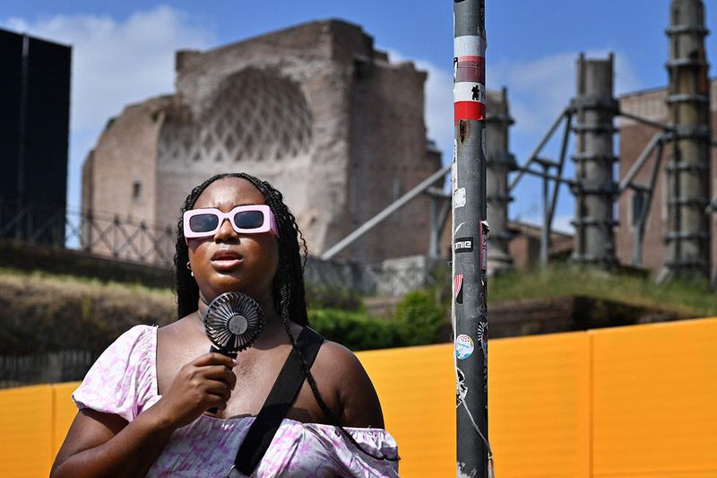 A woman cools off with a mini fan  in Rome, on July 14, 2023, as Italy is hit by a heatwave.