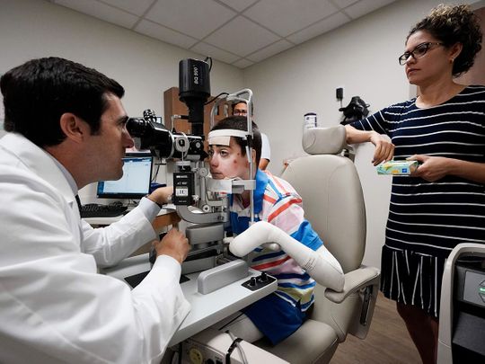 Dr. Alfonso Sabater, left, examines Antonio Vento Carvajal's eyes accompanied by his mother, Yunielkys Carvajal, right, at University of Miami Health System's Bascom Palmer Eye Institute in Miami. 