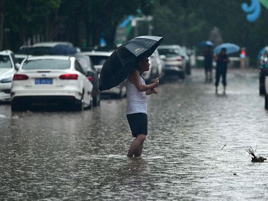 People wade along a flooded street, amid heavy rains in Mentougou district in Beijing on July 31, 2023. Heavy rains battered northern China on July 31, killing at least two people in Beijing while washing away cars and inundating subway stations, with the capital issuing its highest alerts for flooding and landslides.