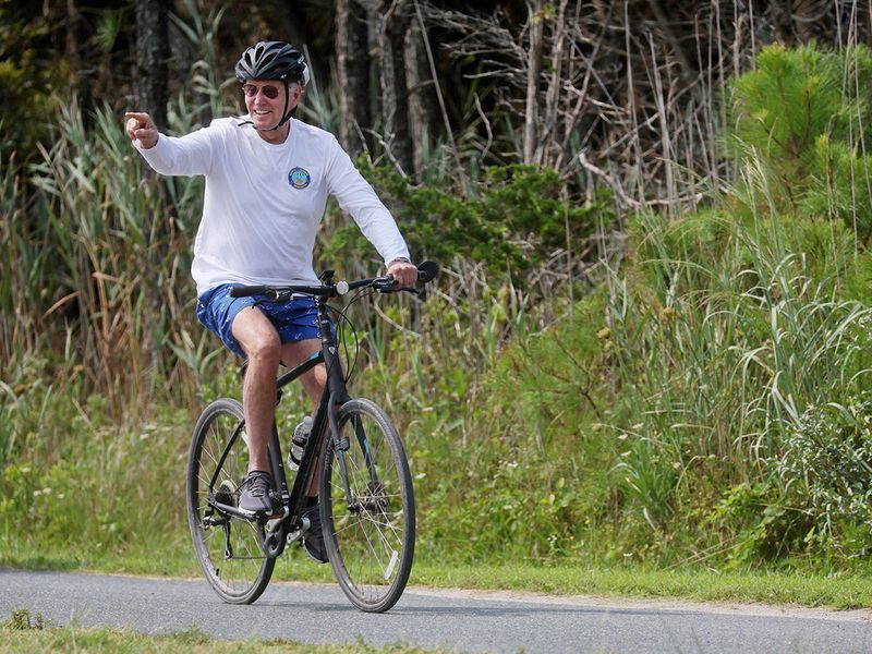 Joe Biden points at onlookers as he rides his bike down a path in Gordons Pond State Park in Rehoboth Beach, Delaware. 