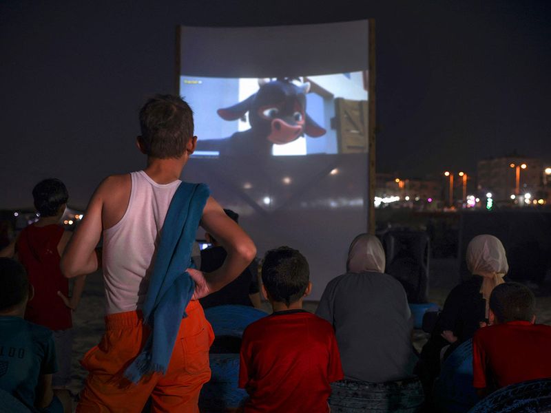 Palestinian children watch a movie at a pop-up open-air cinema at the beach in Gaza city on July 28, 2023, as there are no movie theatres in the blockaded Gaza Strip. 