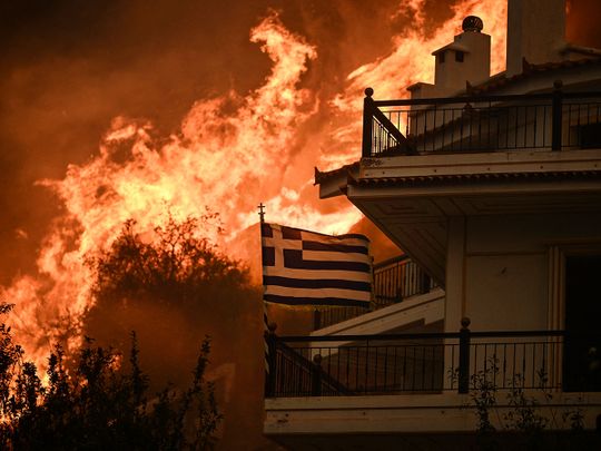 A Greek flag flutters in the wind during a wildfire in Chasia in the outskirts of Athens on August 22, 2023. 