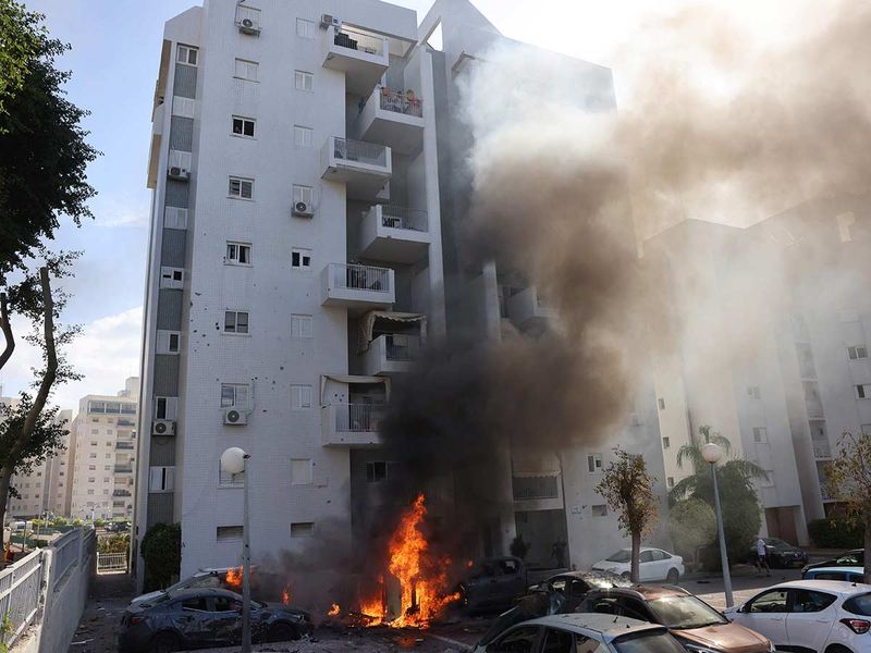 Cars parked outside a residential building catch fire during a rocket attack from the Gaza Strip on the southern Israeli city of Ashkelon, on October 7, 2023.