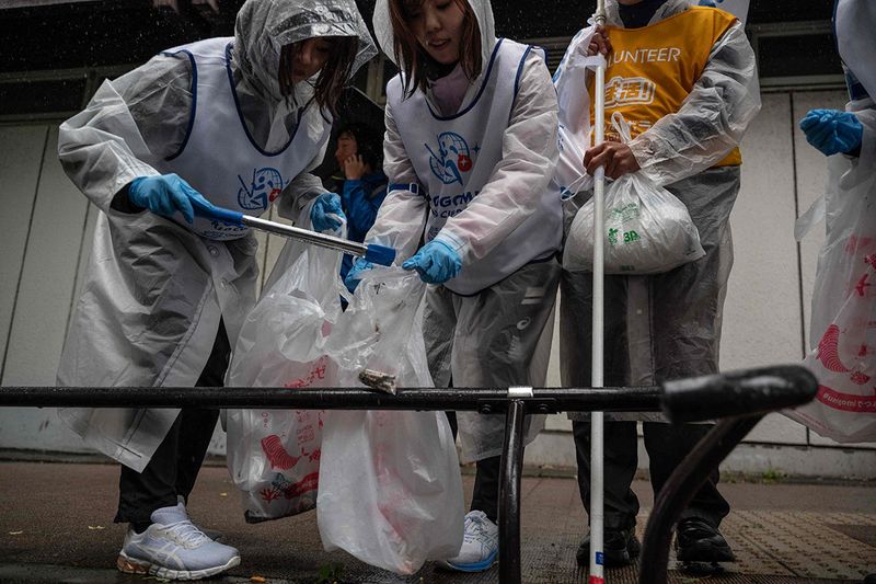 Participants pick up cigarette butts from the street during the Japan stage of the 