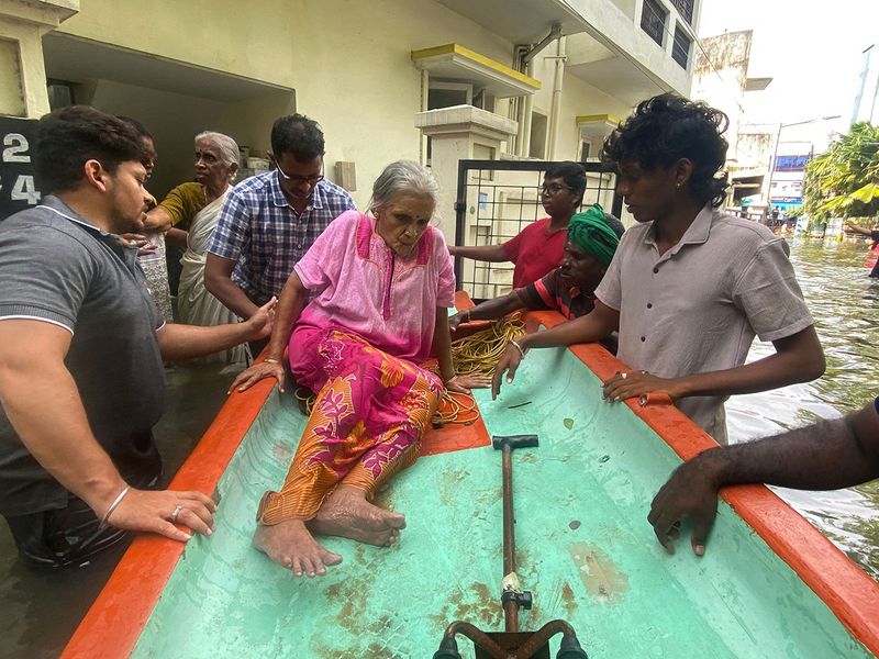 Residents assist an eldery woman to sit on a boat as she is evacuated from her home at a flooded area in Chennai on December 5, 2023, following intense rains after Cyclone Michaung made a landfall. Chest-high water surged down the streets of India's southern city Chennai on December 5, with eight people killed in intense floods as Cyclone Michaung made landfall on the southeast coast. 