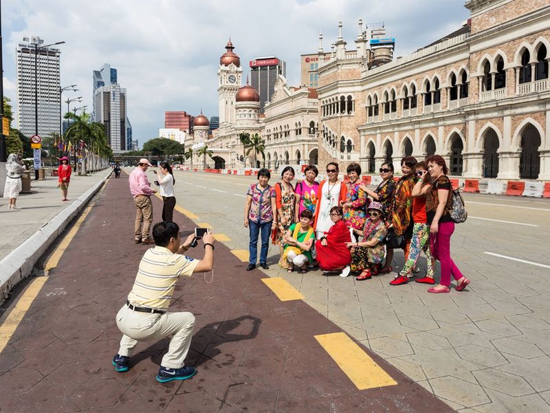 tourists poses for a photo in front of the Sultan Abdul Samad building by Kuala Lumpur Independence (Merdeka) square.  