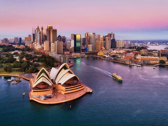 Pinkish colourful sunrise over Sydney city CBD on waterfront of Harbour around Circular quay with major architectural landmarks and symbols of Australia.