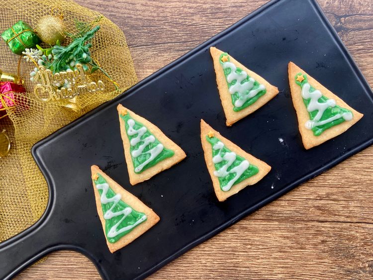 Add green icing to the triangle cookies, leaving the corners empty. Pipe a zigzag string with white icing and place a star sprinkle on top.