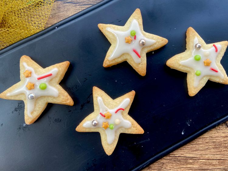 Cool the cookies, mix icing ingredients, pipe icing on star-shaped cookies, decorate with sprinkles.