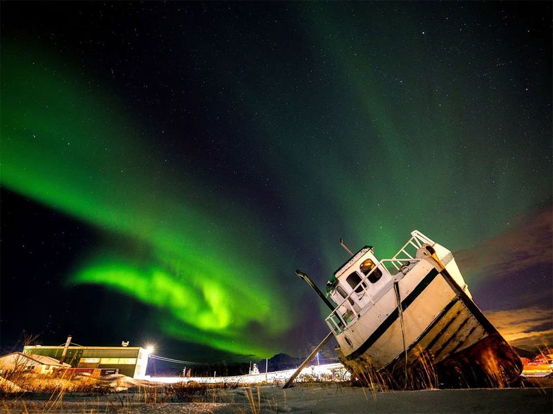 The Northern Lights, also called Aurora Borealis, illuminate the night sky over a boat on the shore in Sommaroy, Norway, November 19. 