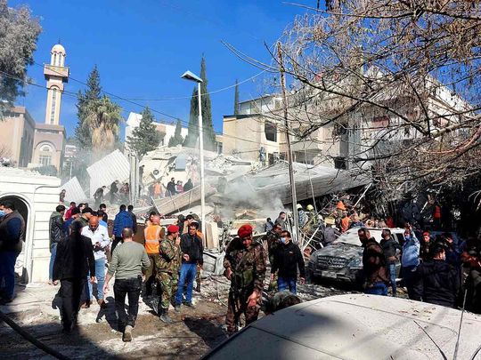 People and security forces gather in front of a building destroyed in a reported Israeli strike in Damascus on January 20, 2024. 