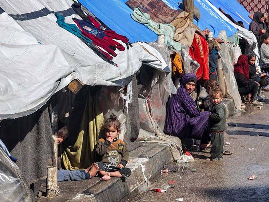 A woman and children sit outside tents sheltering displaced Palestinians in Rafah in the southern Gaza Strip on February 8, 2024, amid the ongoing conflict between Israel and the Palestinian militant group Hamas.
