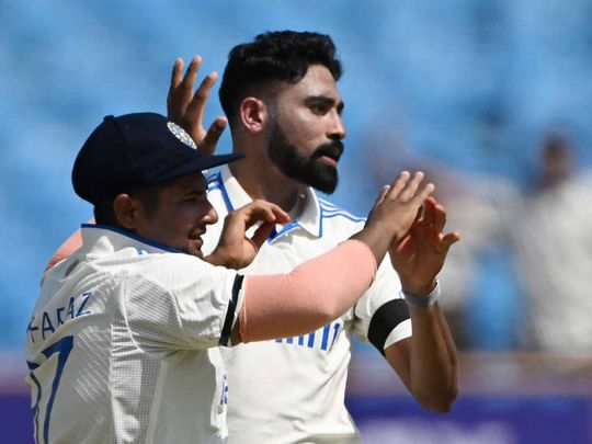 India's Mohammed Siraj (R) celebrates with a teammate after taking the wicket of England's James Anderson during the third day of the third Test cricket match between India and England at the Niranjan Shah Stadium in Rajkot on February 17, 2024.