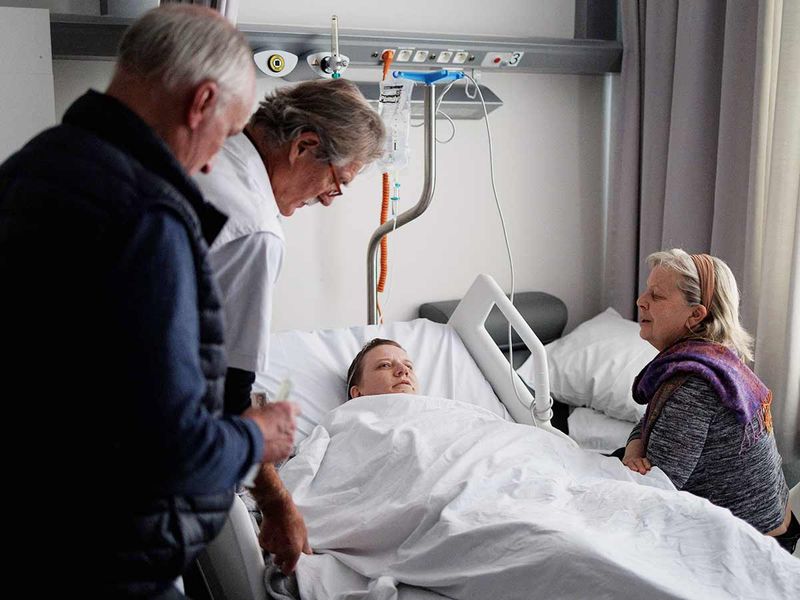Doctor Yves de Locht (L) and Wim Distelmans, Professor in palliative care, arrive in the hospital room for the euthanasia of Lydie Imhoff (C) as her carer Marie-Josee Rousseaux (R) holds her hand at a hospital in Belgium, on February 1, 2024.  