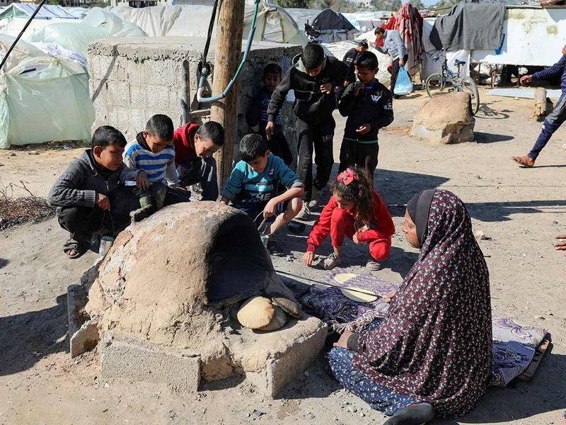 A Palestinian woman bakes bread as children sit next to her, while Gaza residents face crisis levels of hunger and soaring malnutrition, in Khan Younis in the southern Gaza Strip. 