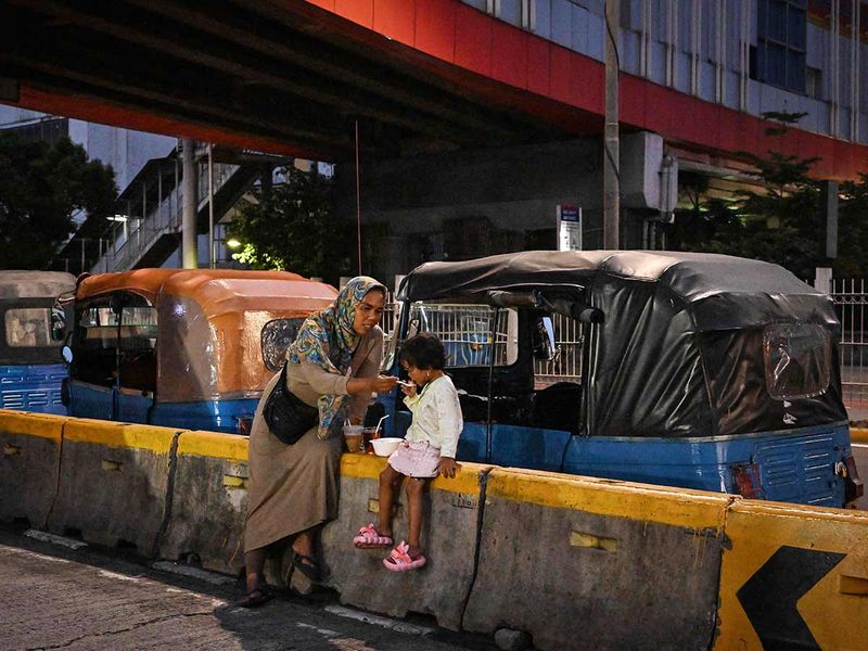 Ekawati feeding her three-year-old daughter Debi by a road divider during a break from their rounds in Jakarta.  