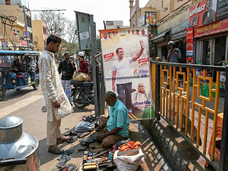 A roadside cobbler sews a shoe beside a poster of India's Congress party leader Rahul Gandhi (L) in Varanasi on March 16, 2024. 