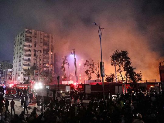 People gather to watch as firefighters battle the flames at the Al Ahram Studio and surrounding buildings in Cairo's Giza district on March 16, 2024.  