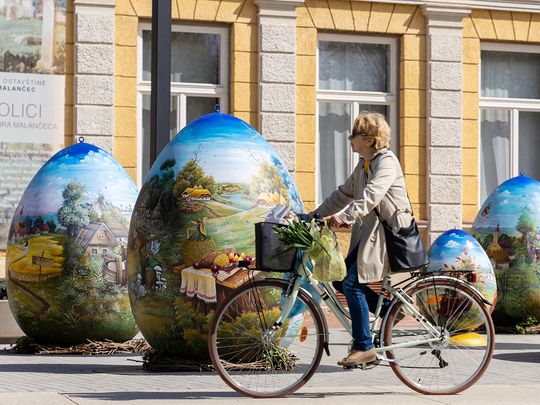 A woman drives on the bike next to sculptures depicting Easter eggs painted in the traditional naive art style in Koprivnica, Croatia. 