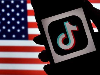 In this photo illustration, the social media application logo, TikTok is displayed on the screen of an iPhone on an US flag background