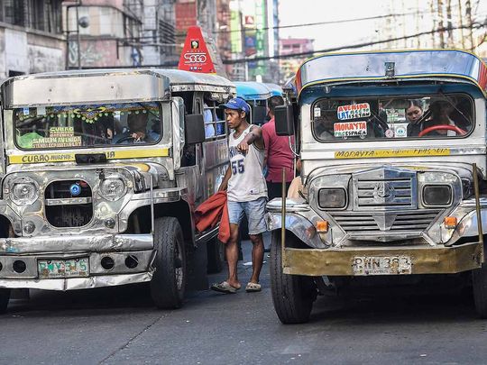 In this photo taken on April 5, 2024, a 'barker' (C), a person who calls passengers to ride jeepneys, guides drivers along a street in Manila.