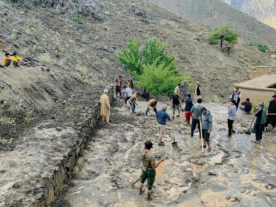 Afghan residents shovel mud following flash floods after heavy rainfall at Pesgaran village in Dara district